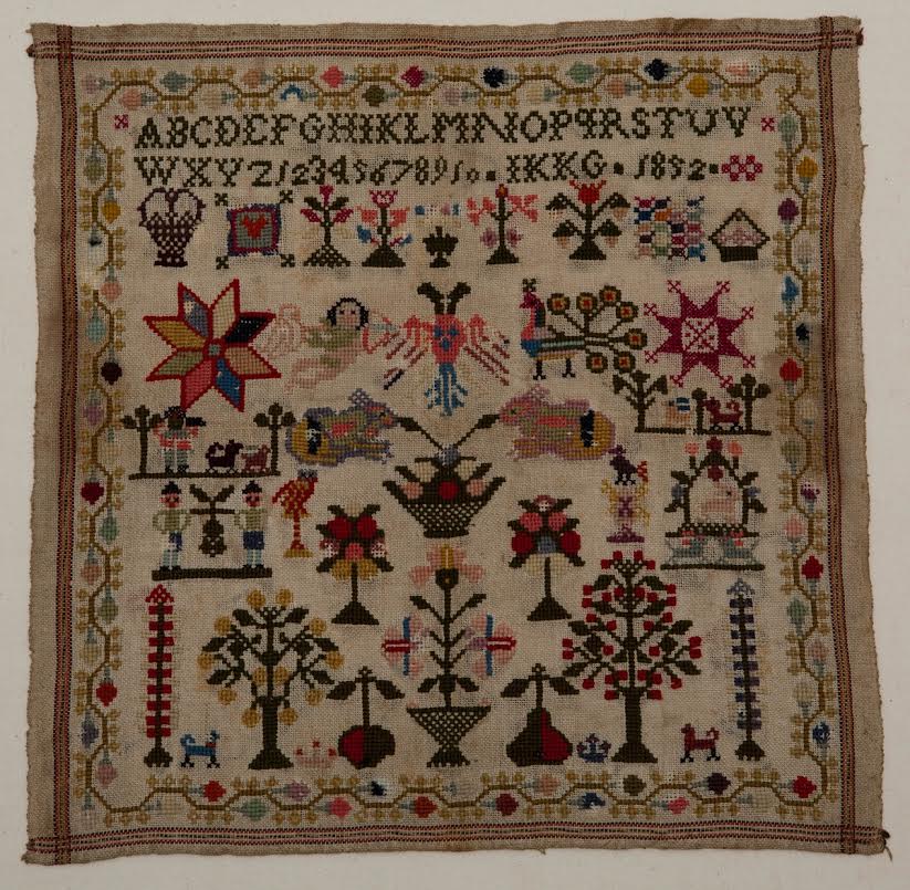 Merklap, kaasdoek met dunne wol geborduurd. Letters en cijfers. Jaartal 1852. Initialen: IKKG. Twee zelfkanten, twee kanten omzoomd. Geborduurd met veel motieven: bloemen, bomen, pauw, sterren, dragers met druiventros.