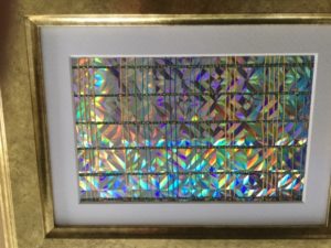 Marijke Jochijms, Glitters. Dit kleine ingelijste werkstuk is geweven in een variatie op de linnenbinding. Het gebruikte materiaal is katoen, blauw glitterdraad en stroken holografisch karton.