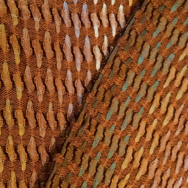 Marijke Jochijms, sjaal. Deze sjaal is geweven in de schijndubbeltechniek. Het gebruikte materiaal is gemerceriseerde katoen in verschillende tinten bruin, beige, groen en geel, geïnspireerd op de herfst en de kleuren van de boombladeren.